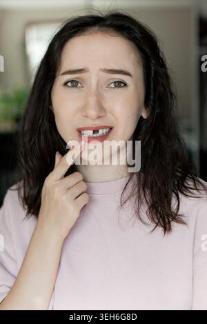 Eine Frau drückt ihre Gefühle aus, nachdem sie einen Vorderzahn verloren hat. Sie berührt ihren Mund in einem Heim. Das Nachmittagslicht zeigt ihr Unbehagen vor einem Stockfoto