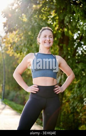 Sportlerin, die nach dem Joggen ausgeruht ist. Frau in Sportbekleidung genießt frische Luft im grünen Park, Zufriedenheit, Ausdauertraining, gesunder Lebensstil, Motivationskonzept Stockfoto