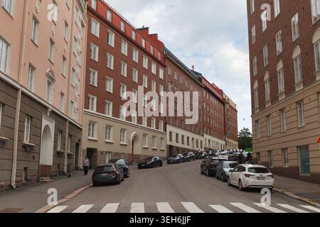 HELSINKI, FINNLAND - 11. AUGUST 2025: Gerade Wohnstraße mit hohen Wohnblocks aus Backstein und Fußgängerüberquerung im Sommer. Stockfoto