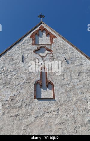 Detailliertes Giebelende der mittelalterlichen Steinkirche mit dekorativen Backsteinnischen und einem kleinen Kreuz auf der Spitze. Stockfoto
