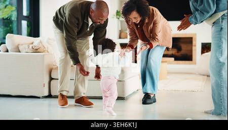 Eltern, Baby und freuen sich auf die ersten Schritte in der Lounge mit Unterstützung, Beifall oder Meilenstein in der Familie zu Hause. Menschen, Mutter und Vater mit Kindern Stockfoto
