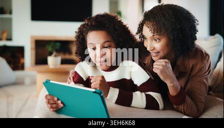 Glücklich, Mutter oder Kind mit Tablet auf Sofa für Unterhaltung, Bonding oder Online-Abonnement zu Hause. Mutter, Tochter oder Kind, das mit Technologie lügt oder Stockfoto