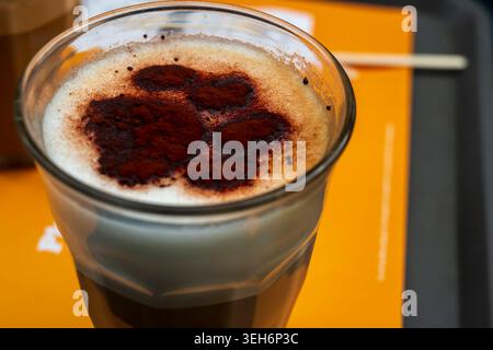 Nahaufnahme eines köstlichen Cappuccino in einem Glas, dekoriert mit einem Kakaopulver-Bärenmotiv in einem Café Stockfoto