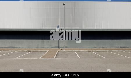 Außenwand aus grauem Beton in der unteren Seite und Aluminiumverkleidung in der oberen Seite, mit einer Straßenleuchte. Porphyr-Gehweg, Parkplatz und Straße Stockfoto
