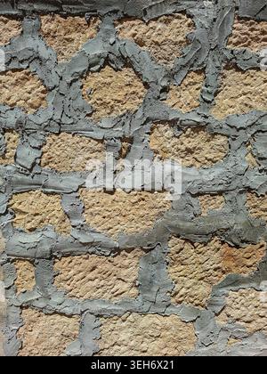 Sonnenlicht scheint auf eine Wand aus rauen Sandsteinblöcken, die von dickem grauen Mörtel zusammengehalten werden. Die Wand zeigt Anzeichen von Alterung und Witterung. Stockfoto