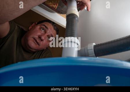 Ein Mann repariert ein Sanitär-Problem unter einer Küchenspüle Stockfoto