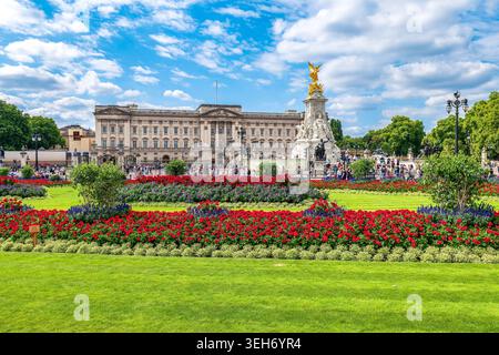 Buckingham Palace und das Victoria Memorial aus einem Landschaftsgarten mit roten Blumen und grünem Rasen in London, Großbritannien. Stockfoto