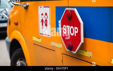 Eine Nahaufnahme der Seite eines hellgelben Schulbusses mit einem roten Stoppschild und einem Warnschild, das anzeigt, dass Kinder anwesend sind. Stockfoto