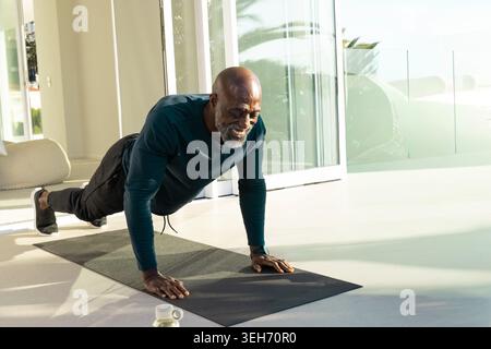 Senior afroamerikanischer Mann, der zu Hause Liegestütze auf Matte trägt und Sportswear und Smartwatch trägt Stockfoto