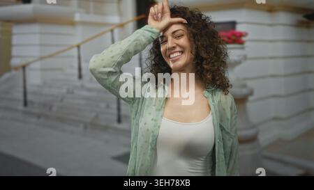 Frau, die mich mit Hand bis Stirn auf Treppen im Freien signiert, breites Lächeln mit Zähnen; verspielt. Stockfoto
