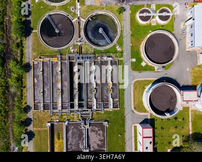 Die Ansicht zeigt eine Wasseraufbereitungsanlage mit großen kreisförmigen Tanks und Aufbereitungsanlagen. Grünflächen umgeben das Gebiet, die städtische Entwicklung zeigen Stockfoto