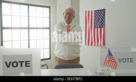 Mann mit überkreuzten Armen, mit einem „ich stimmte“-Sticker, neben einem klaren Wahlzettel und amerikanischer Flagge in einem Wahlhaus, Stolz auf die bürgerliche Pflicht. Stockfoto