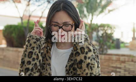 Frau mit runder Brille und Leopardenmantel lächelnd mit dem Kopf nach hinten geneigt und den Fingern in der Nähe von Schläfen auf einer Straße; verspielte Freude. Stockfoto