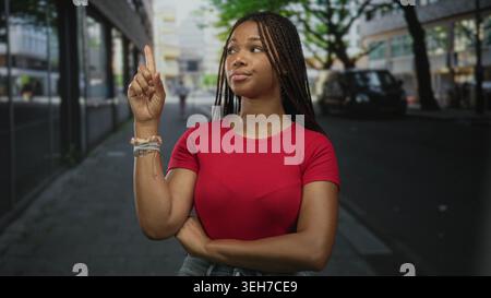 Frau zeigt mit überkreuzten Armen und sichtbaren Armbändern den Zeigefinger auf die Straße; Selbstbewusstsein. Stockfoto