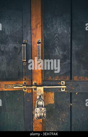 Nahaufnahme eines verwitterten Vorhängeschlosses auf einem rostigen Metallriegel einer dunklen Holztür, die auf nebeligen Wiesen sitzt: Ali Bedni Bugyal, Chamoli, Uttarakhand, Indien. Stockfoto
