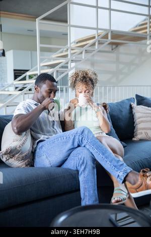Verschiedene Paare sitzen eng auf einem marineblauen Sofa mit gemusterten Kissen im Wohnzimmer und halten Tassen. Modern, gemütlich, Freundschaft, Entspannung, Inneneinrichtung, Lifestyle, minimalistisch Stockfoto