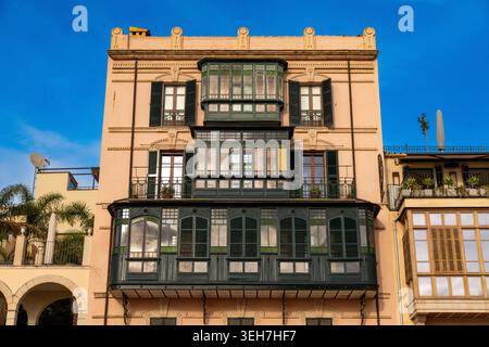 Palma - Balearen - Spanien - 01-01-2026: Fassade eines hellen Gebäudes mit grünen geschlossenen Balkonen, Fensterläden und eisernen Geländern, beleuchtet durch wenig Sonnenlicht unter blauem Himmel. Stockfoto