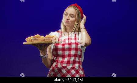 Die Chefin im Studio hält hölzerne Muffins mit Hand und Finger bis Kinn, um Gebäck zu untersuchen; Nachsicht. Stockfoto