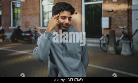 Mann in grauem Kapuzenpullover zeigt mit dem Finger auf den Tempel auf der Kopfsteinpflasterstraße neben geparkten Fahrrädern und Backsteintüren; nachdenklich. Stockfoto
