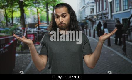 Der Mann zuckt mit den Palmen in der Stadtstraße mit erhobenen Schultern und sichtbaren Unterarmen; Unentschlossenheit-Dilemma. Stockfoto