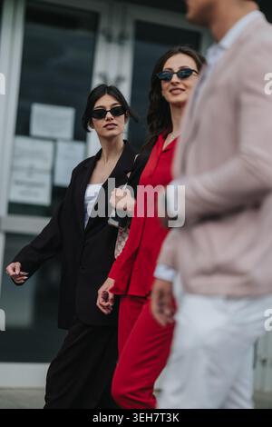 Drei stylische Profis, die zusammen in Sonnenbrille und Geschäftskleidung durch die Stadt laufen Stockfoto