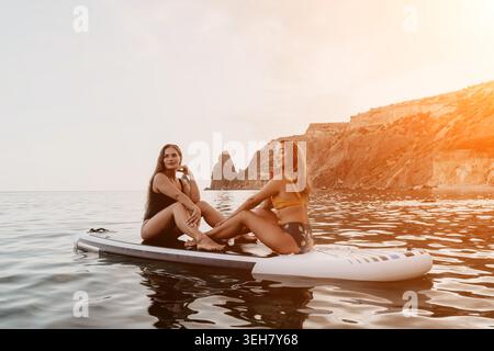 Paddleboard, Women, Ocean - zwei Frauen, die sich auf einem Paddleboard im Meer entspannen und einen Tag am Strand genießen. Stockfoto