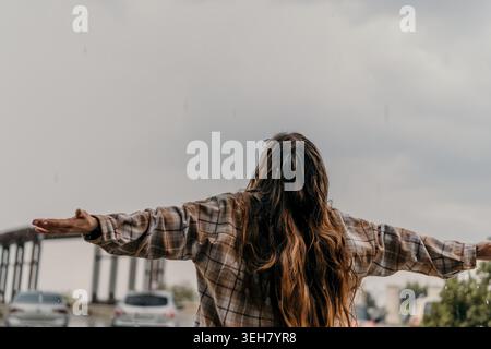 Frau Regenfreiheit Frau stehend mit ausgestreckten Armen unter einem bewölkten Himmel während des Regens mit Kopierraum Stockfoto