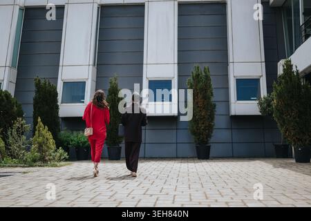 Zwei Geschäftsfrauen, die zusammen in ein modernes Bürogebäude in urbaner Umgebung gehen Stockfoto