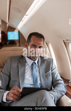 Geschäftsmann, der auf Geschäftsreisen an einem Tablet in einer privaten Jet-Kabine arbeitet Stockfoto