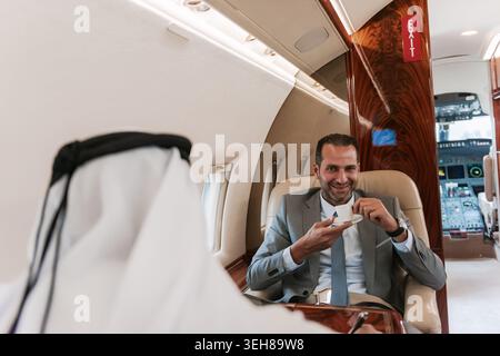 Geschäftsmann genießt Kaffee während eines Meetings an Bord eines Privatjets mit luxuriösem Interieur Stockfoto