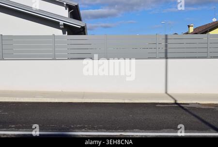 Hauszaun aus grauem Metallgeländer an weißer Gipswand. Betonfußweg und Straße vor dem Hotel, Himmel auf dem Hintergrund. Hintergrund für Kopierbereich Stockfoto