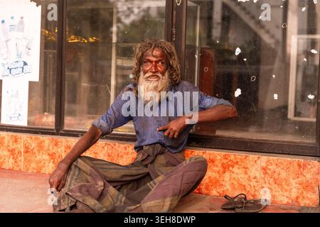 Sri Lanka - 14. Januar 2026: Blick auf einen älteren Mann mit langen, verfilzten Haaren und einem Bart, der ein blaues Hemd und Sarong trägt, während er vor einem Glas sitzt Stockfoto