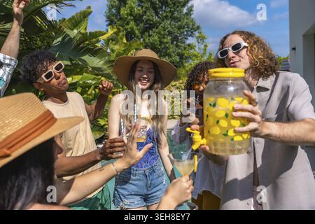 Verschiedene Gruppen junger Freunde, die eine sonnige Poolparty genießen, lächeln und mit erfrischenden Limonaden und Cocktails rösten, während sie sich entspannen und gesellig machen Stockfoto