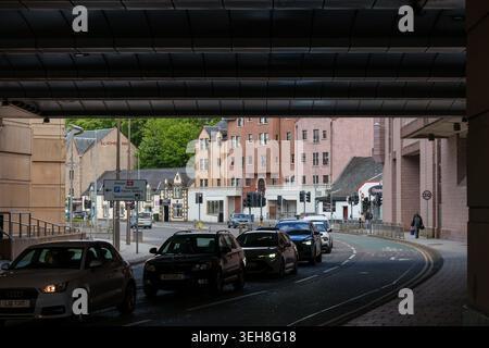 Der Verkehr bewegt sich entlang einer Stadtstraße in Inverness, Highlands and Islands, Schottland, mit mehreren Gebäuden und einem Fußgänger. Stockfoto