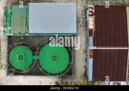 Aus der Vogelperspektive zwei große grüne Lagertanks und Industriegebäude mit Wellblechdächern in Hanimaadhoo, Haa Dhaalu Atoll, Malediven. Stockfoto