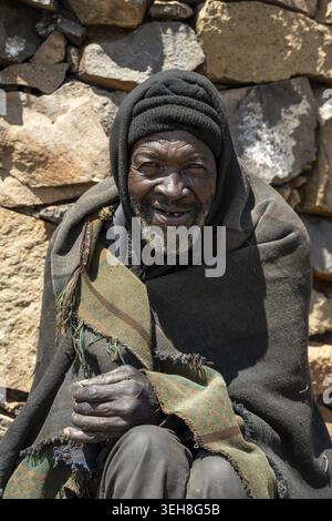 Porträt eines älteren Mannes in warmer Kleidung, der vor einer Steinmauer sitzt, Königreich Lesotho, Lesotho Stockfoto