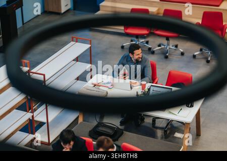 Geschäftsmann, der an einem Laptop arbeitet, in einem modernen Coworking Space mit roten Stühlen Stockfoto
