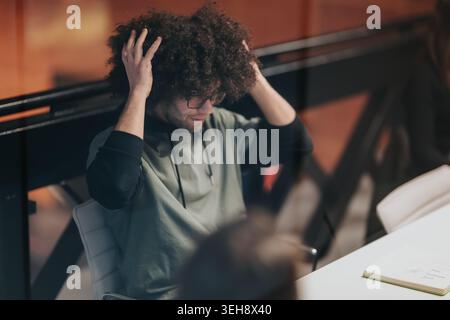 Junger Mann mit lockigen Haaren und Brille, die sich in einem modernen Besprechungsraum anpasst Stockfoto