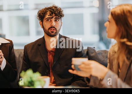 Junger Geschäftsmann, der bei einem zwanglosen Treffen mit Kollegen bei einem Kaffee aufmerksam zuhört Stockfoto