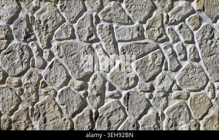 Rustikale Steinwand mit hellbeigen Felsen auf weißem Zement. Hintergrund und Textur. Stockfoto