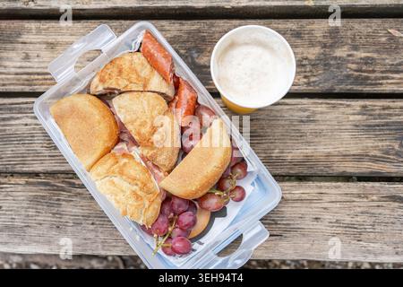 Snack-Set für ein Picknick während einer Reise im Freien. Sandwiches, Würstchen und leichtes Bier auf einer rauen Holztischoberfläche, Freizeit- und Campingkonzept. Stockfoto