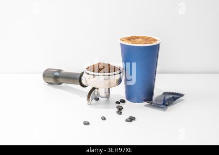 Ein rustikaler Pappbecher mit einer gewellten Hülle wird zwischen zwei Handschuhen gehalten, während das Ventil ein Tropfen Dampf abgibt, der sich mit der ra vermischt Stockfoto
