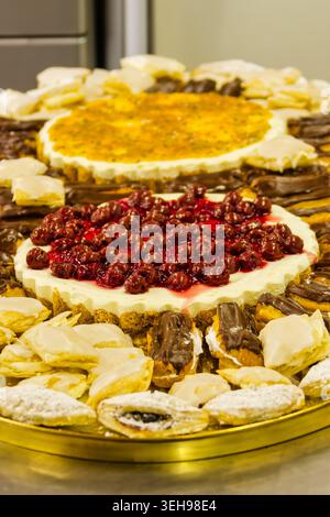 Große Auswahl an Desserts Käsekuchen mit Kirschglasur und ganzen Kirschen, umgeben von mehreren schokoladenglasierten Eclairs, präsentiert Stockfoto