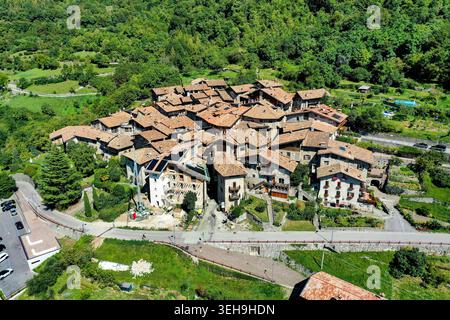 Blick aus der Vogelperspektive auf das mittelalterliche Steindorf Canale di Tenno mit traditionellen Terrakotta-Dächern, eingebettet zwischen üppigen grünen Hügeln in Ville del Monte, T Stockfoto