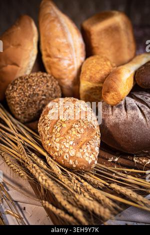Eine rustikale Mischung aus frisch gebackenem, handwerklichem Brot mit Samenbrötchen und dunklem Vollkornbrot, umgeben von goldenen Weizenstielen. Stockfoto