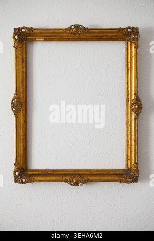 Ein goldener Bilderrahmen hängt an einer weißen Wand. Der Rahmen ist leer und enthält kein Bildmaterial oder Foto. Stockfoto
