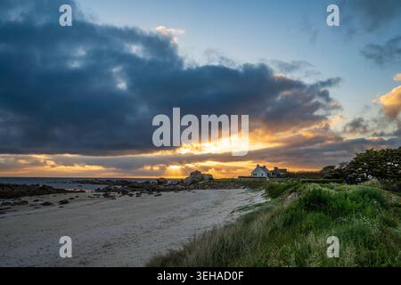 Eine spektakuläre aufgehende Sonne erleuchtet die zerklüftete Küste von Finistère. Warmes Licht filtert durch Wolken über dem weißen Sandstrand und Granitfelsen, mit einem Stockfoto