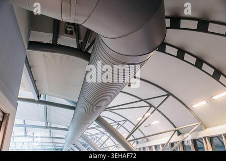 Weitwinkelblick auf einen großen Lüftungskanal aus Metall und gebogene Deckenbalken in einem modernen Innenraum, der Industriedesign und strukturelle Geom unterstreicht Stockfoto