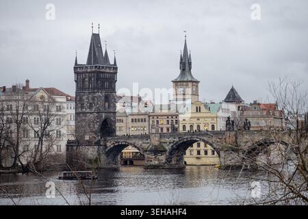 Besucher spazieren entlang der Karlsbrücke und genießen dabei den Blick auf den Brückenturm und die umliegenden Gebäude in Prag. Die Szene fängt einen bewölkten Tag b ein Stockfoto