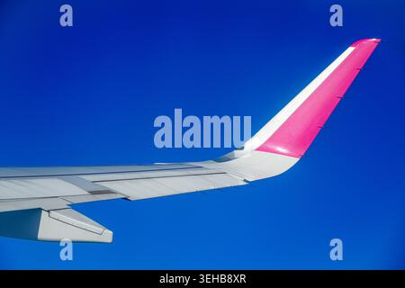 Flugzeugflügel im Flug mit blauer und purpurpurroter Lackierung gegen Himmel und Boden Hintergrund Stockfoto